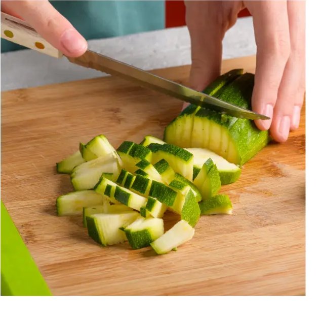 Hands slicing a green zucchini on a wooden cutting board